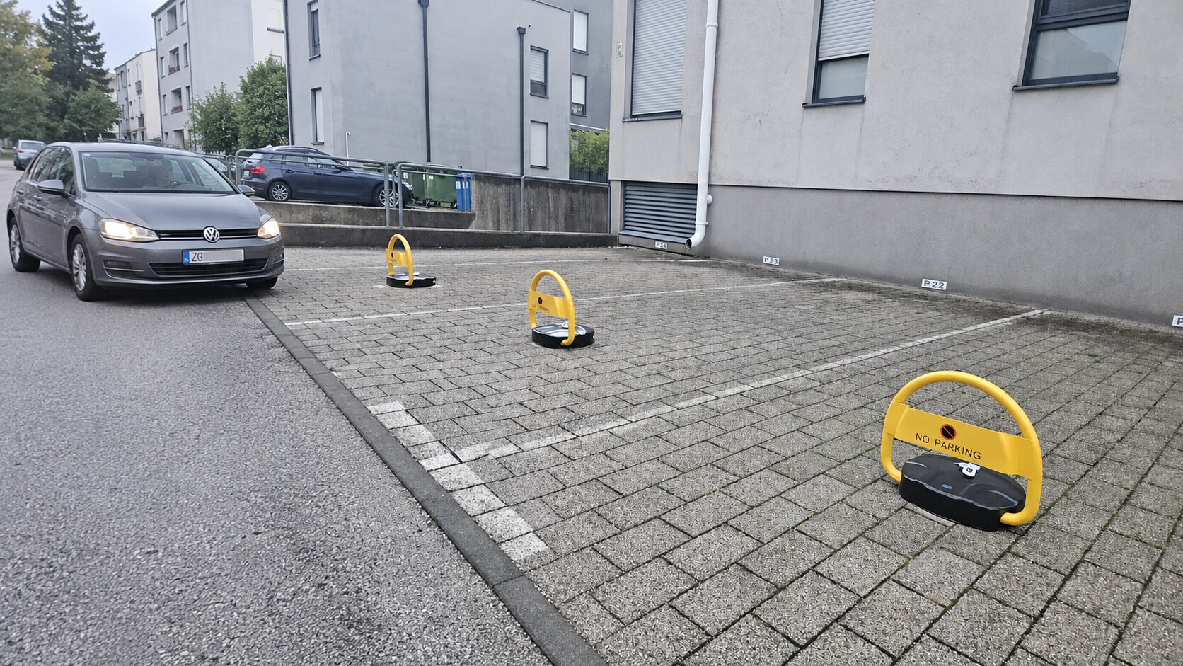 Parking barijere čuvaju dostupnost mjesta uz zgradu Tri žute parking barijere na mjestima uz zgradu